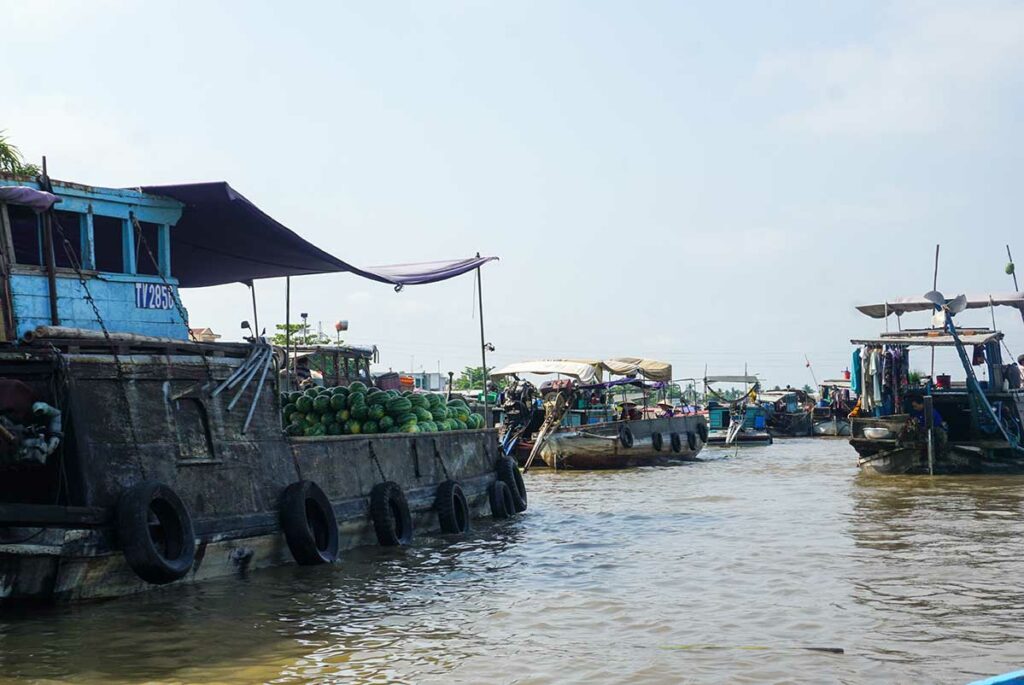 Trading boats at Cai Rang Floating Market with piles of watermelons on deck and buyers in smaller sampans collecting produce.