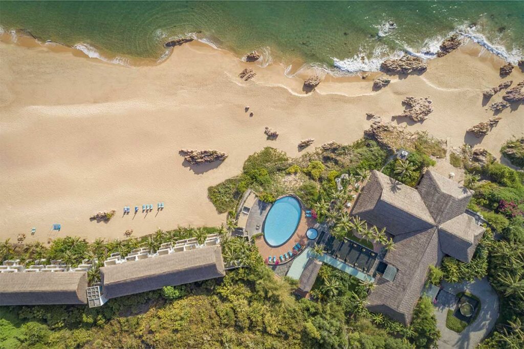 Aerial view of Avani Quy Nhon Resort and Bai Xep Beach – Wide sandy bay with rocky outcrops, turquoise water, and a resort pool blending into the coastal scenery.