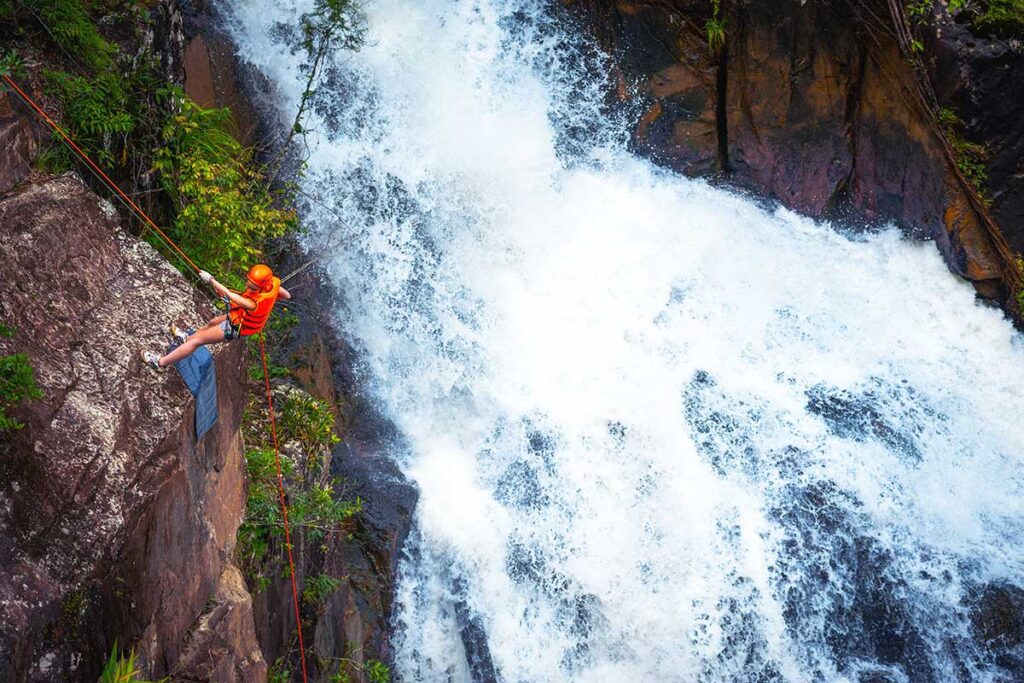 A man abseiling down a cliff next to a waterfall as part of canyoning in Dalat.