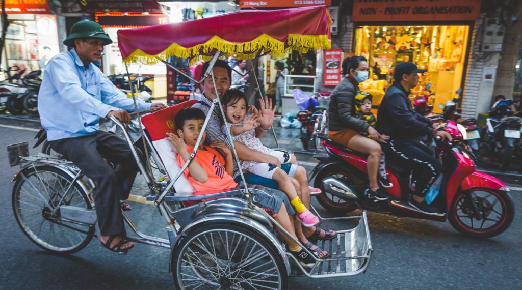 Two kids sitting with their dad in a cyclo tour in Hanoi