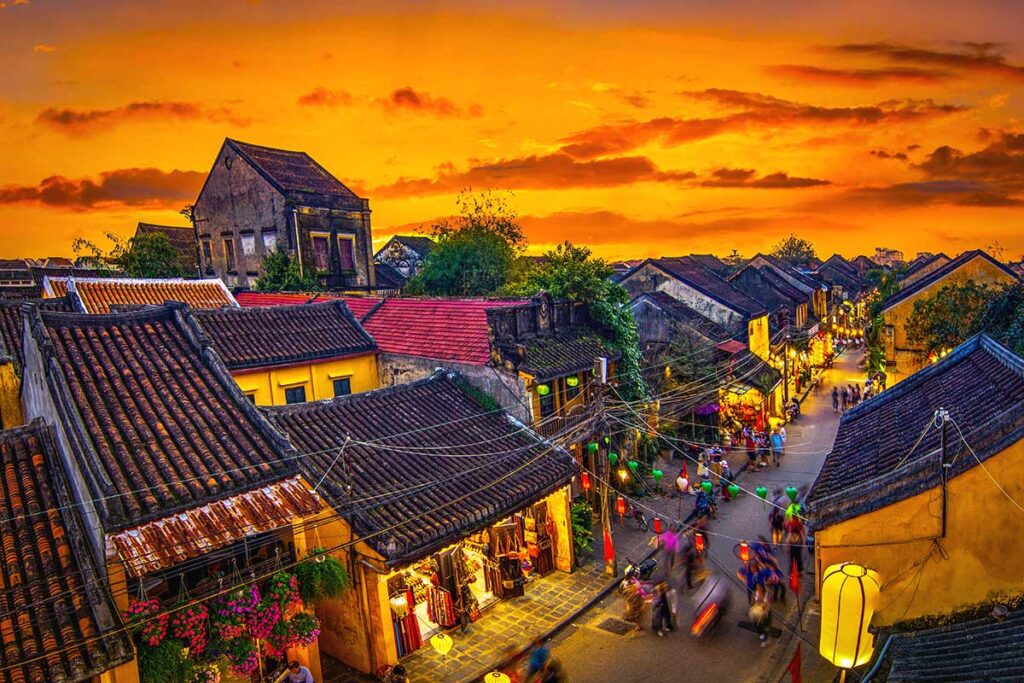 A view of the ancient town of Hoi An at sunset, creating a golden hue sky above the tiled roofs of the old houses.