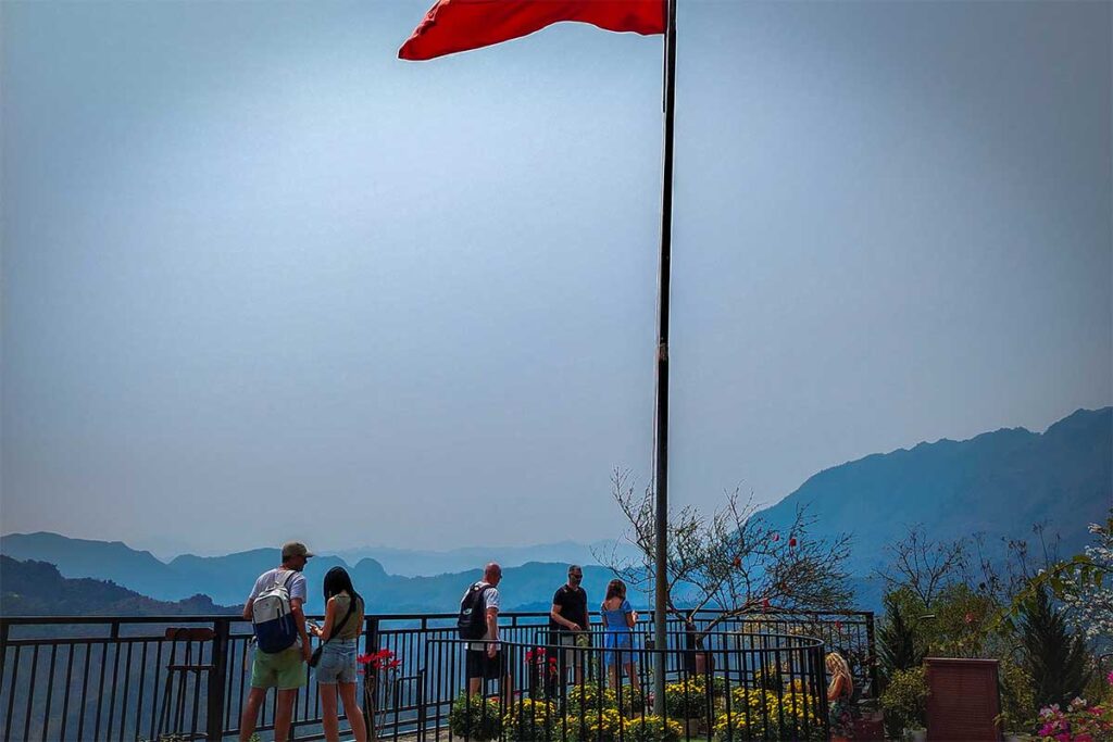 A flag at Thung Khe Flagpole (also called Mai Chau Viewpoint) with people enjoying the view from the railing 
