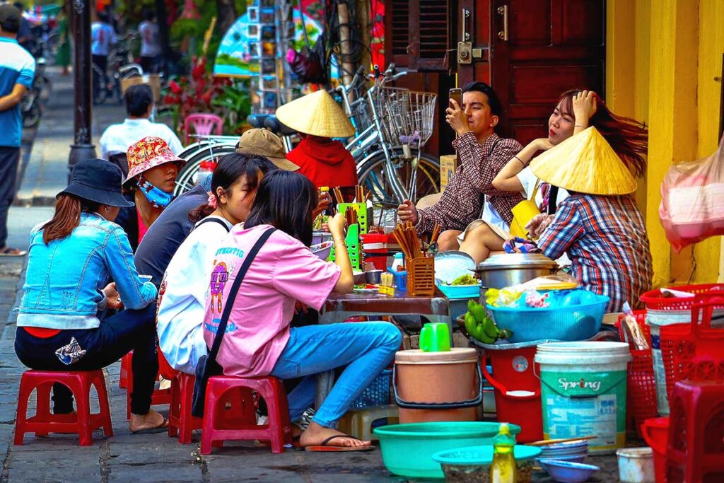 Locals in Hanoi sitting on the street on low plastic stools enjoying local street food.