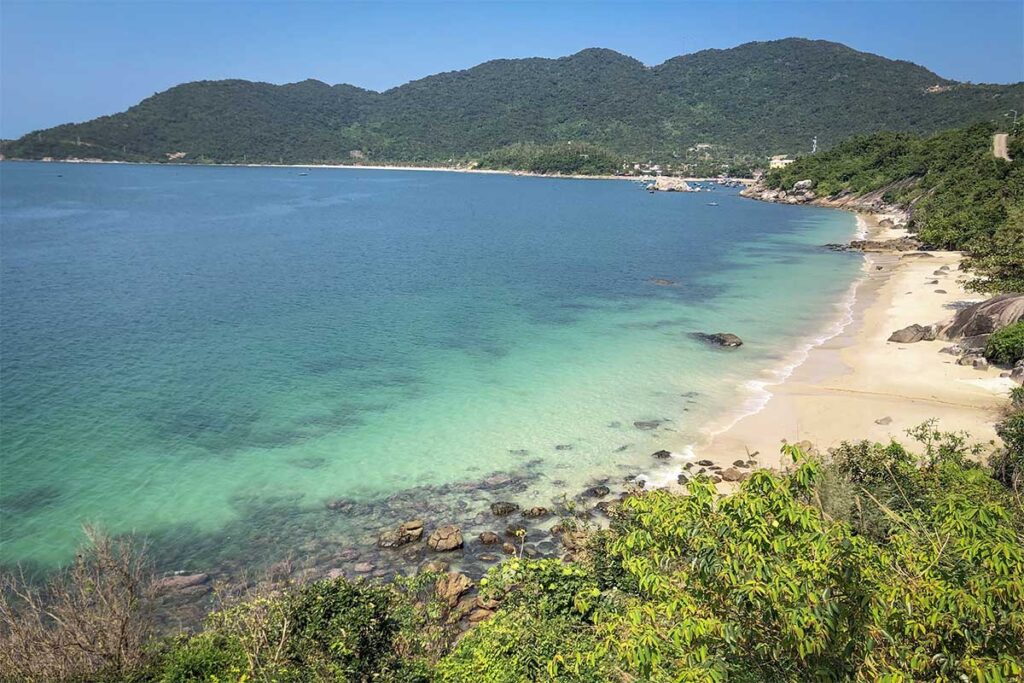 Hidden Bai Xep Beach on Cham Island, a quiet cove surrounded by green hills and shallow blue water.