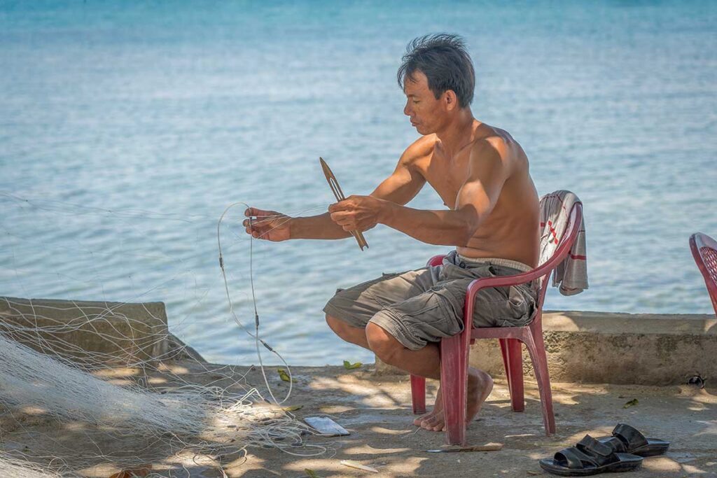 Fisherman repairing a net by the sea on Cham Island, part of the island’s daily coastal life and traditional livelihoods.