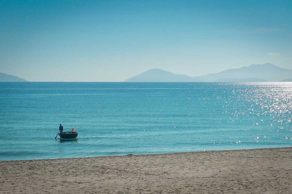 Local fisherman rowing a traditional round basket boat on the turquoise sea off Cua Dai Beach