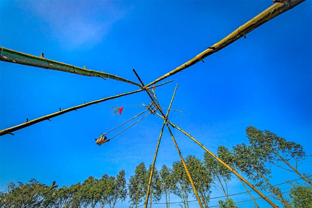 A man sitting on a large bamboo swing setup for the Du Tien Festival