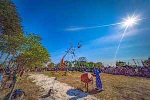 A man in blue traditional clothes is hitting a large drum with in the background a giant bamboo swing that is used for Du Tien Festival in Hue