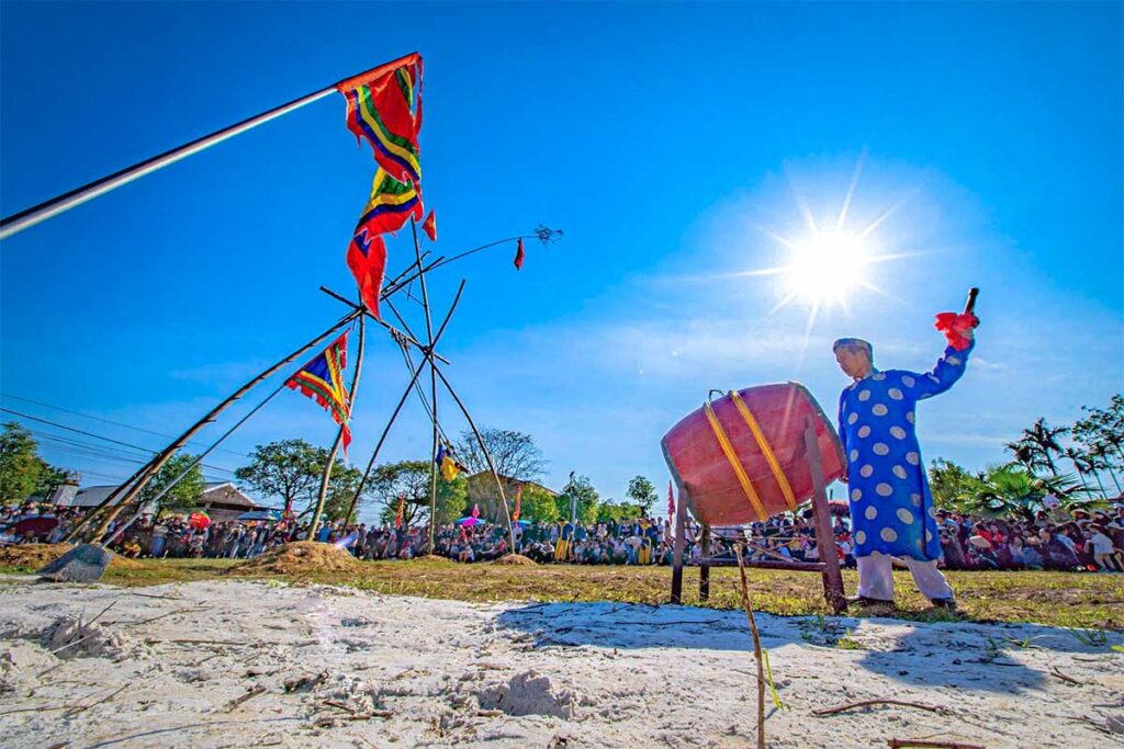 A man with historical clothes hitting a large drum during Du Tien Festival with in the background a giant bamboo swing