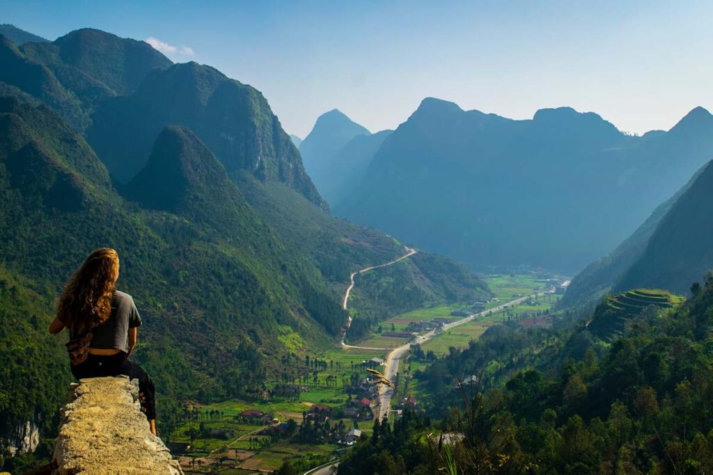 Clear skies and warmer weather in Ha Giang, with a girl sitting in her shirt watching the view of mountain scenery