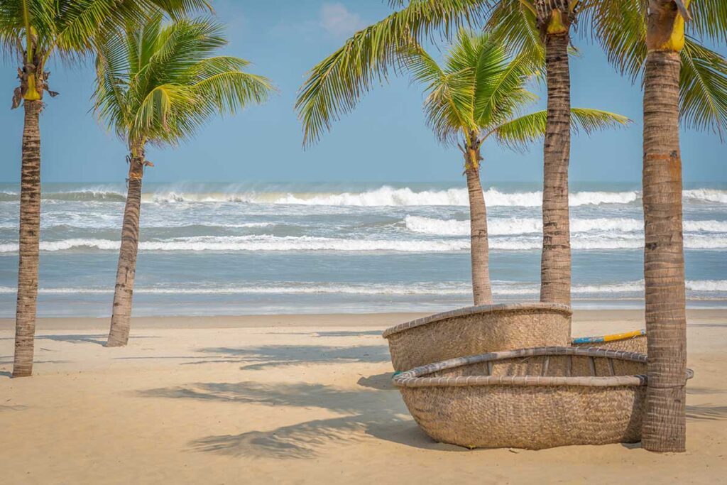 Thatched sun loungers under palm trees on An Bang Beach, one of the best beaches in Hoi An, Vietnam.