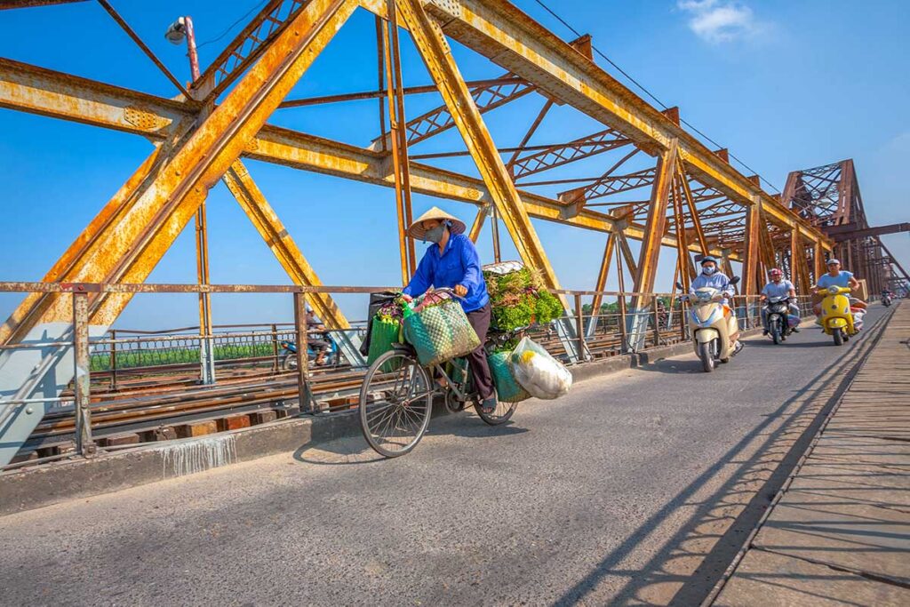 Motorbikes and a local on a bicycle are crossing the Long Bien Bridge in Hanoi