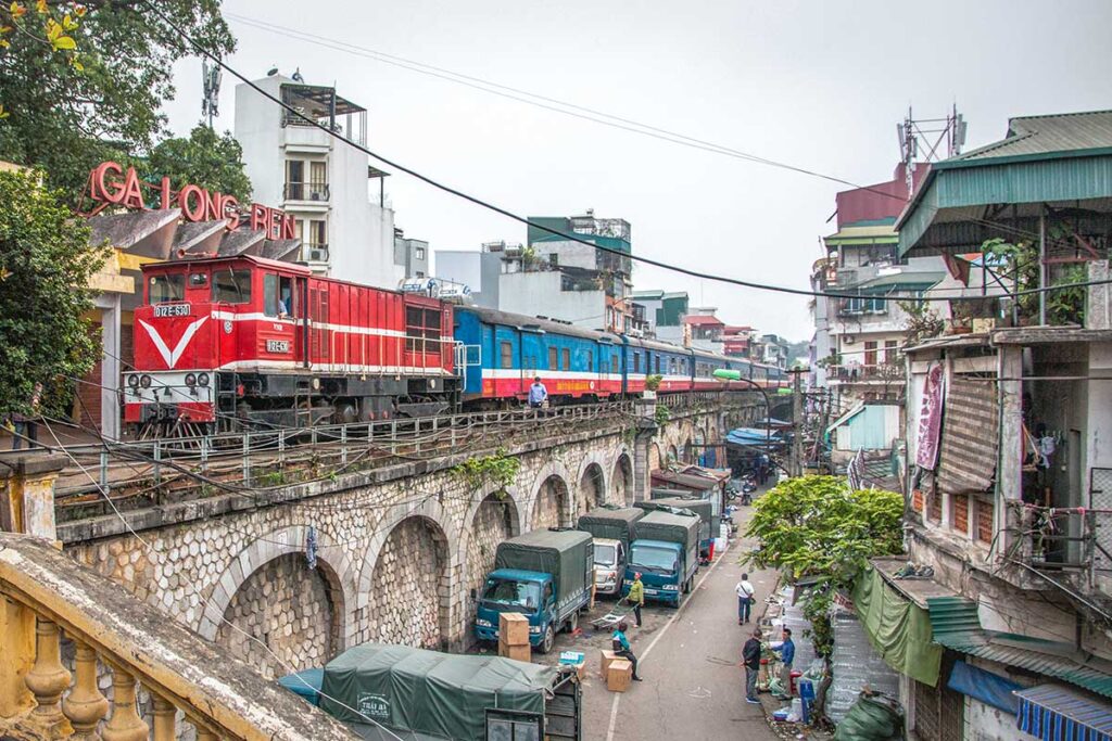 A train is passing by Long Bien Railway Station with also views of a local street of Hanoi