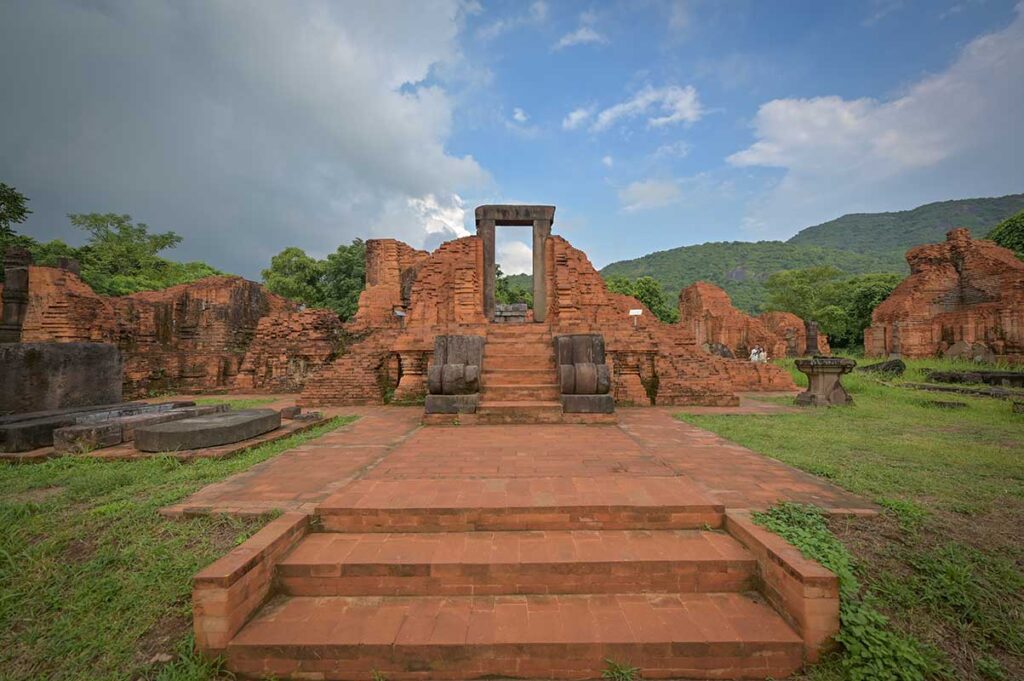 “Restored foundations and main entrance of a Cham temple in Group A at My Son Sanctuary, with red brick steps and surrounding hills.