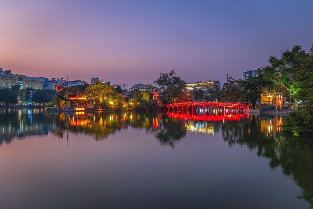 View of Ngoc Son Temple on Jade Island and The Huc Bridge in the late evening with lights turned on creating a beautiful effect with reflections on Hoan Kiem Lake