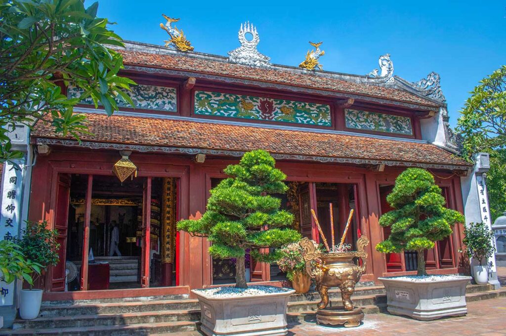 Front view of Ngoc Son Temple hall with incense burner and bonsai trees