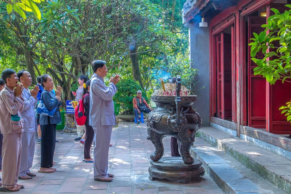 Locals praying with incense in front of the main temple hall at Ngoc Son Temple