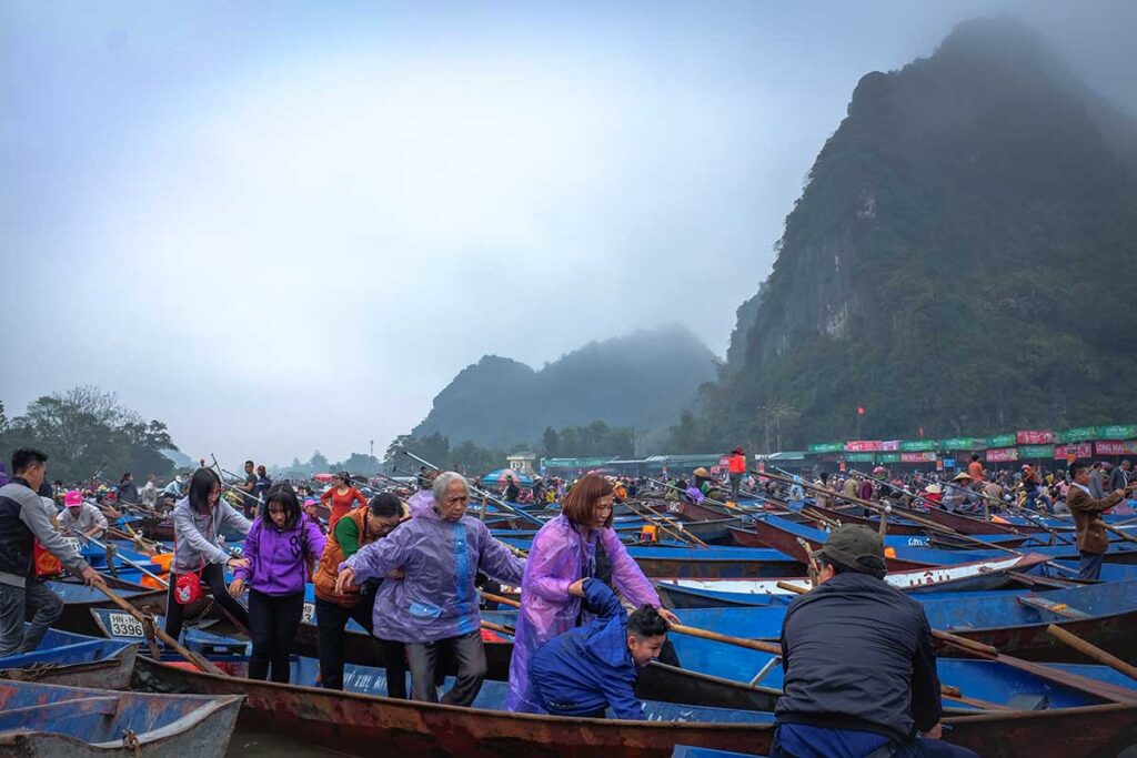 Many rowing boats docked at the wharf on the Yen River with crowds finding their boats to get to the temple complex during Perfume Pagoda Festival
