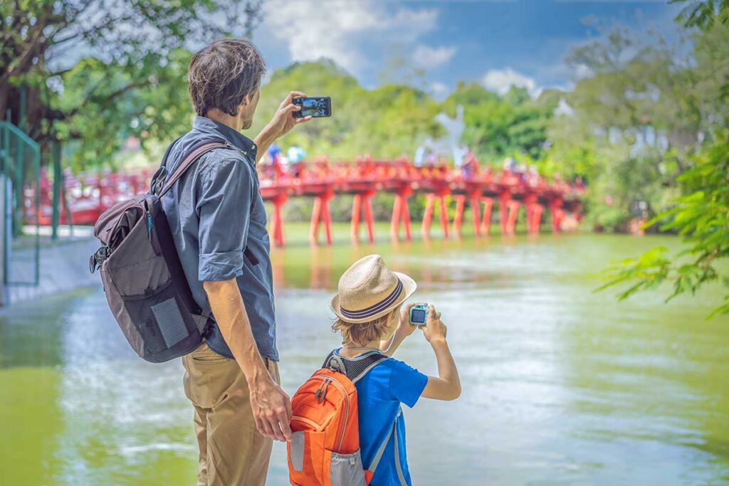 A farther and son are making a photo of The Huc Bridge seen from the lakeshore 