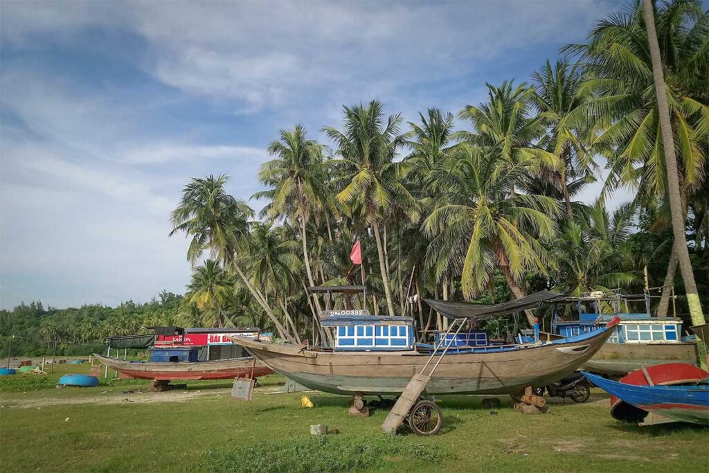 Fishing boats resting on the grass under palm trees on Tam Hai Island, showcasing everyday coastal life in central Vietnam.
