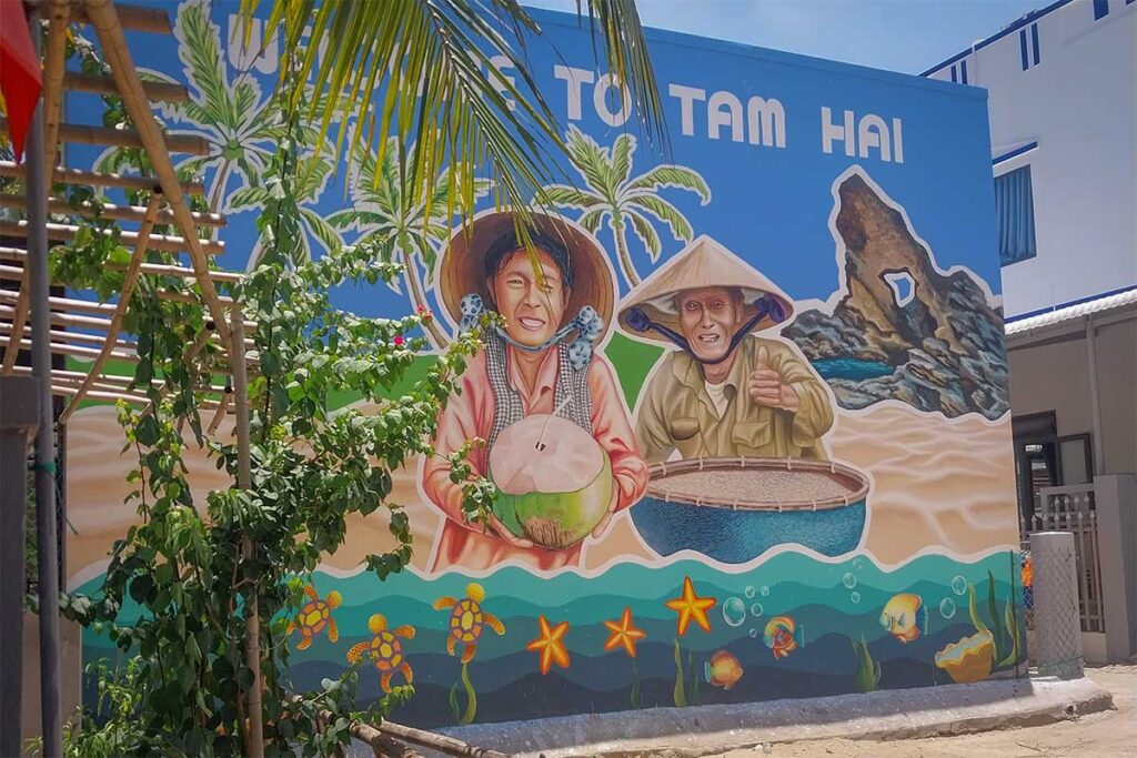 Colorful mural in Tam Hai Island’s mural village depicting local fishermen and coconut sellers, with Ban Than rock formations in the background.