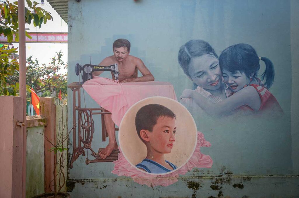Mural of a tailor and family scene at Tam Thanh Mural Village, depicting everyday Vietnamese life through community art in Quang Nam Province.
