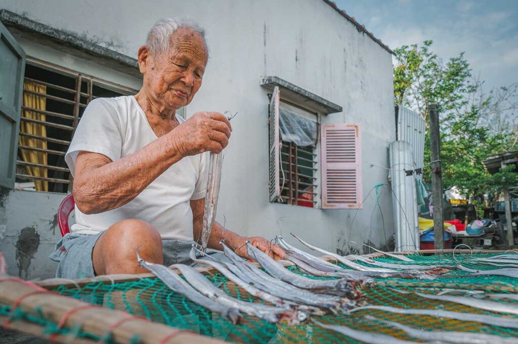 Elderly fisherman in Tam Thanh Mural Village preparing fish outside his home — a glimpse of traditional coastal life in central Vietnam’s fishing communities.