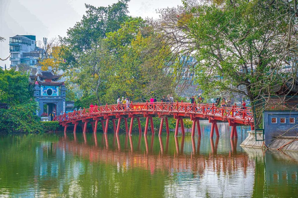 The Huc Bridge seen from lakeshore where the iconic red bridge reflects in the water of Hoan Kiem Lake