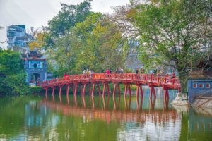 The Huc Bridge seen from lakeshore where the iconic red bridge reflects in the water of Hoan Kiem Lake