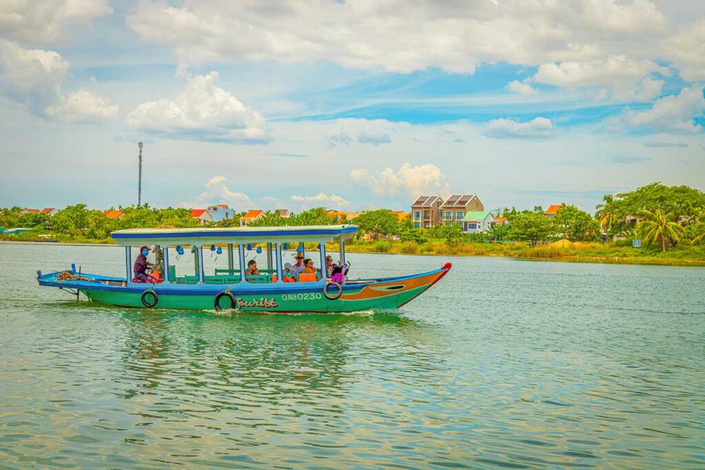 Colorful wooden boat carrying travelers on a scenic cruise along the Thu Bon River near Hoi An, a popular add-on after visiting My Son Sanctuary.