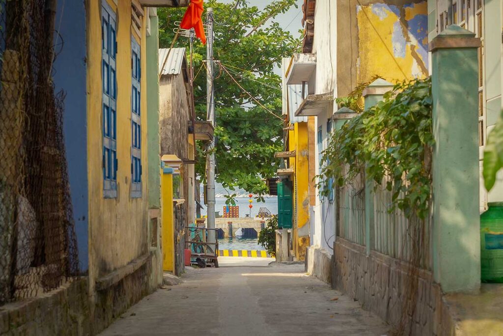 Narrow alley in Bai Lang village on Cham Island with colorful houses leading toward the sea and fishing pier.