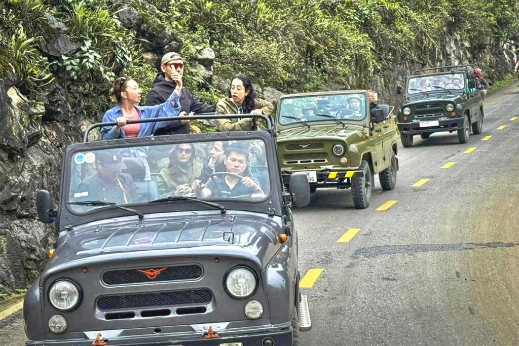 Tourists on an open jeep tour in Ha Giang standing and admiring the stunning mountain scenery.