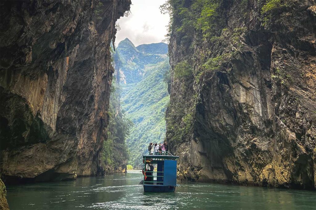 The Nho Que River winding through Khau Vai Canyon, with a boat carrying tourists between towering cliffs.