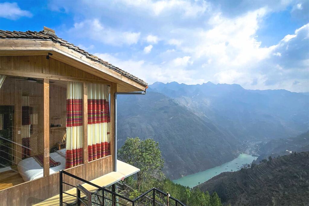 A cozy bungalow-style room with large windows and a bed facing the stunning mountain views of Ma Pi Leng Pass.  