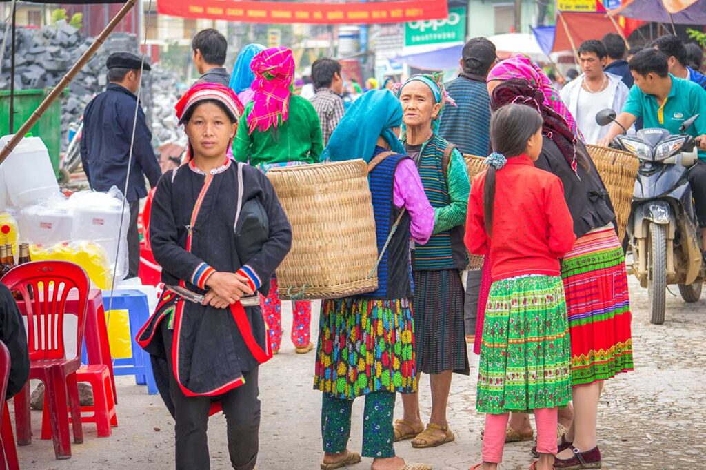 A group of ethnic women in colorful traditional clothing chatting at Meo Vac Market.