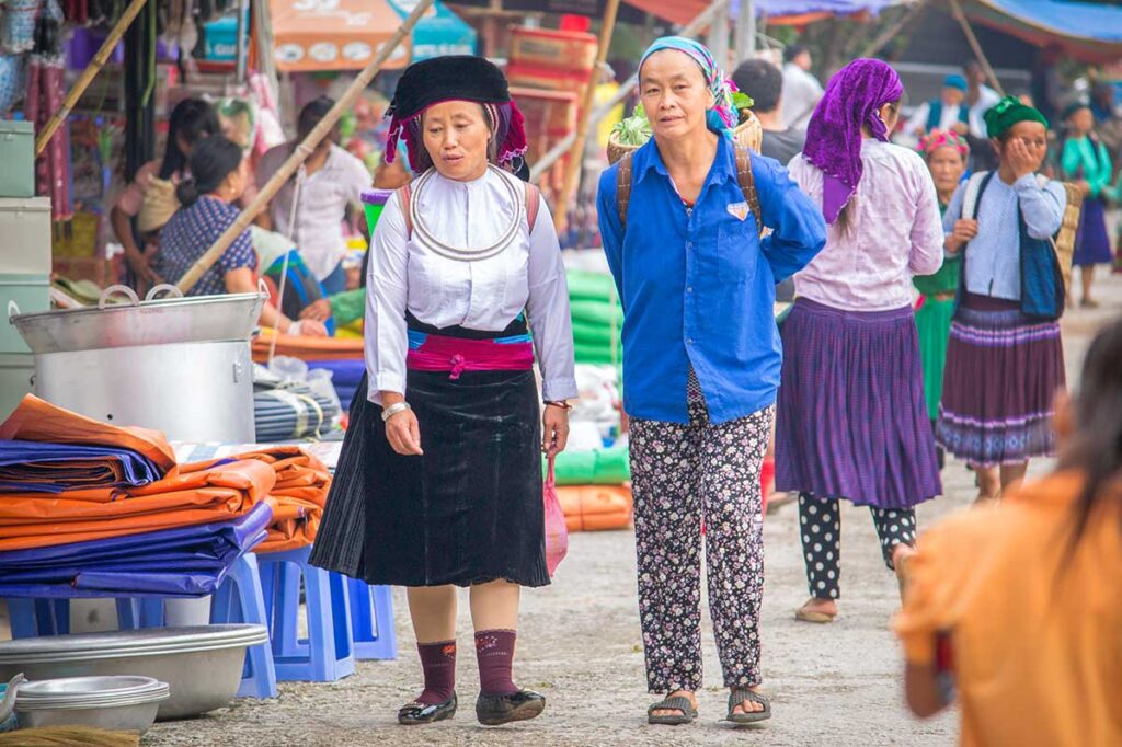 Two ethnic women walking through Meo Vac Market, one carrying a basket on her back.