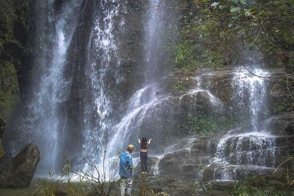 A girl standing on a rock, gazing at the Nam Dam Waterfall cascading down the mountainside.