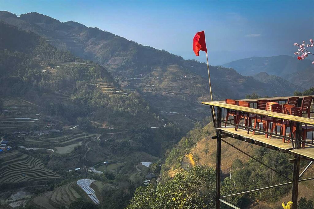 Café with a view at Ta Muong Village – A small, basic café with red plastic chairs overlooking breathtaking mountain scenery and terraced rice fields at Ta Muong Village viewpoint in Ha Giang.