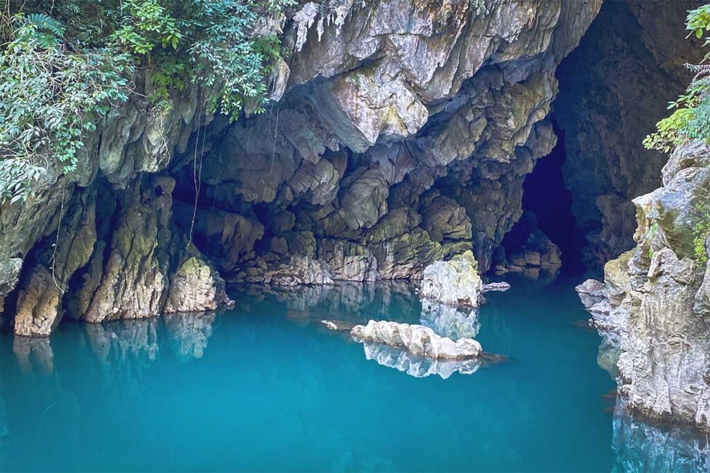 Emerald blue water at Tham Lin Cave – A stunning view of the clear, emerald-blue waters inside Tham Lin Cave, surrounded by lush greenery in Ha Giang.
