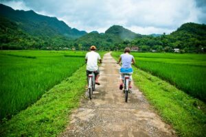 Two people on a countryside road are cycling in Mai Chau between the green rice fields