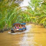 Tourist boat ride through canals in Ben Tre – Group of travelers cruising under dense nipa palms on a Mekong Delta waterway.