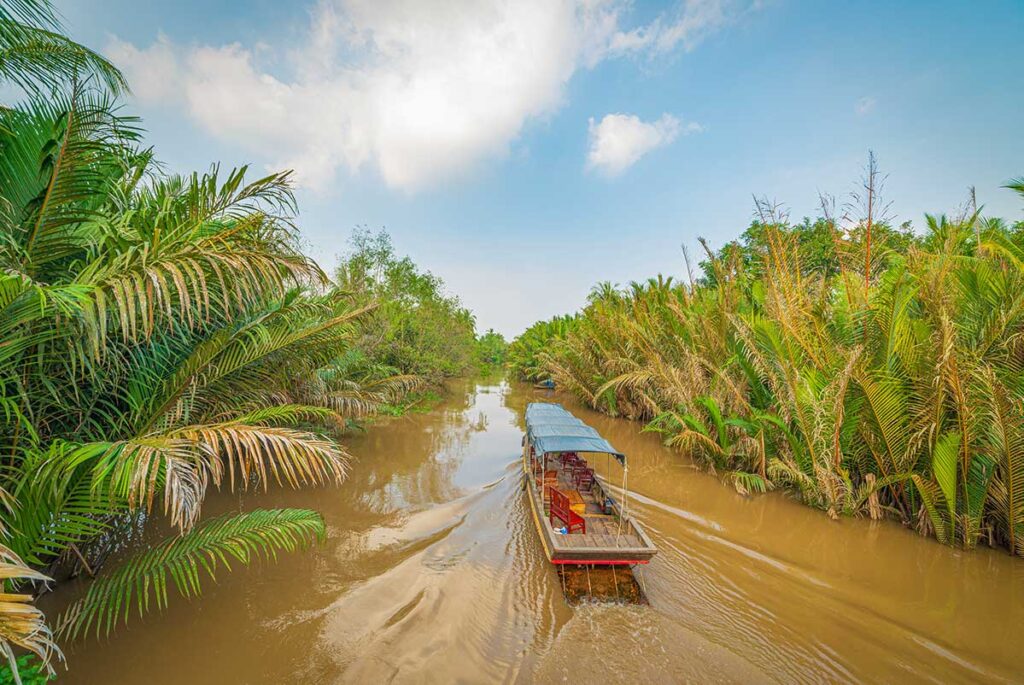 Wooden boat cruising a quiet Ben Tre canal – Scenic waterway lined with nipa palms in the Mekong Delta.