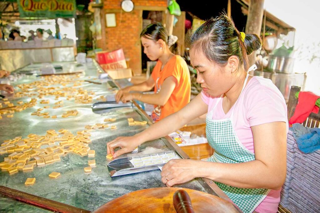 Coconut candy making in Ben Tre – Women cutting and wrapping freshly made coconut candy at a traditional workshop in Ben Tre, Mekong Delta, Vietnam.