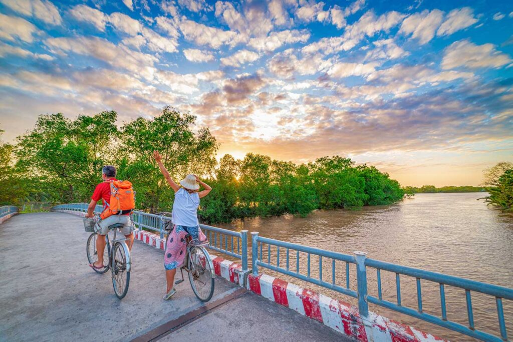 Tourists cycling across a bridge at sunset in Ben Tre, Vietnam, overlooking the Mekong Delta’s peaceful waterways.