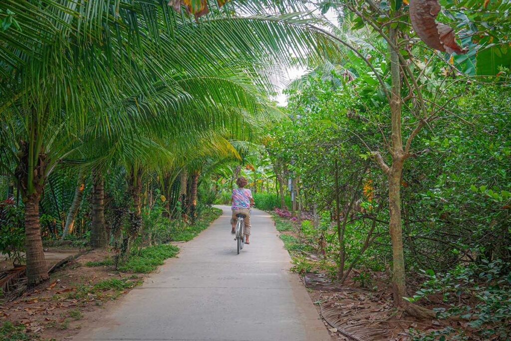 Cyclist riding through a palm-shaded village path in Ben Tre, Vietnam – one of the best ways to experience local life in the Mekong Delta.