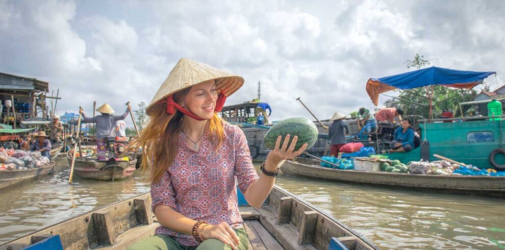 Traveler wearing a conical hat holding a watermelon on a boat ride at Cai Rang Floating Market in Can Tho.