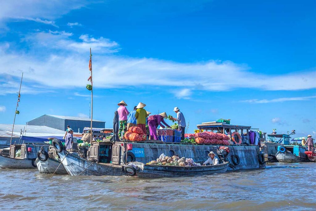 Wholesale boats at Cai Rang Floating Market stacked with onions and pumpkins, with vendors transferring produce between boats.