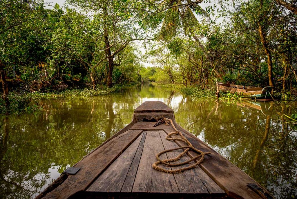 Front view of a wooden boat navigating a peaceful canal surrounded by greenery near Can Tho