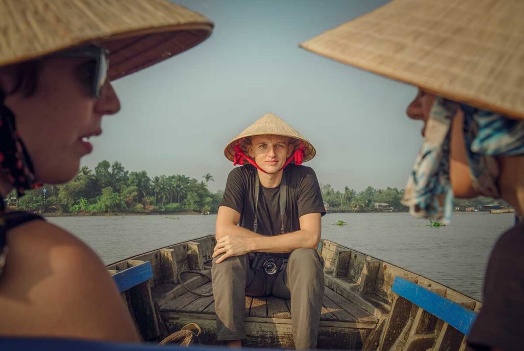 Tourist wearing conical hat enjoying a local boat ride on the Hau River in Can Tho