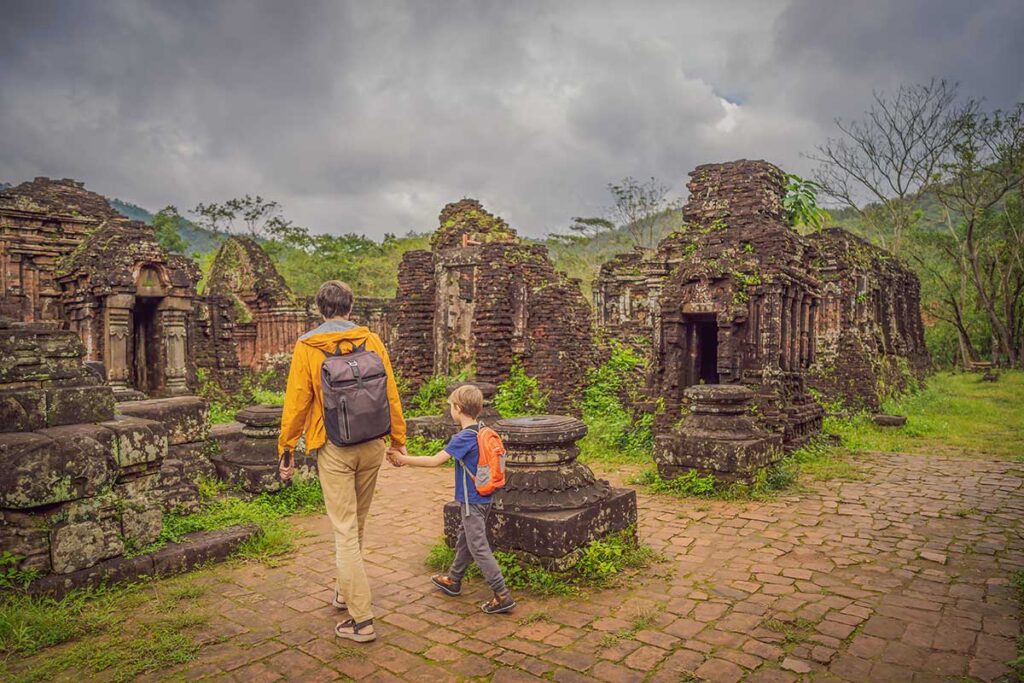 A father and his son walk hand in hand through the ancient brick ruins of the My Son temples near Hoi An, an easy half-day trip on a family holiday in Vietnam with kids.